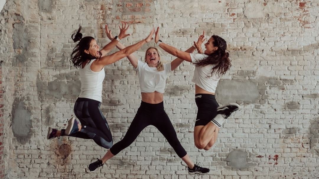 Drie sporters springen tegelijk omhoog voor een bakstenen muur